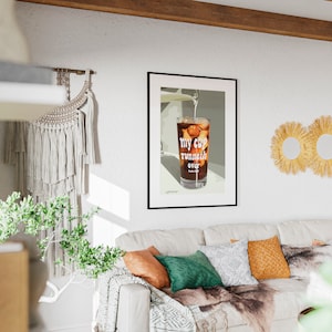 Pu&ograve; includere: Una stampa incorniciata di un bicchiere di caff&egrave; freddo con il testo "my cup runneth over" in un soggiorno con un divano bianco, una coperta e cuscini.