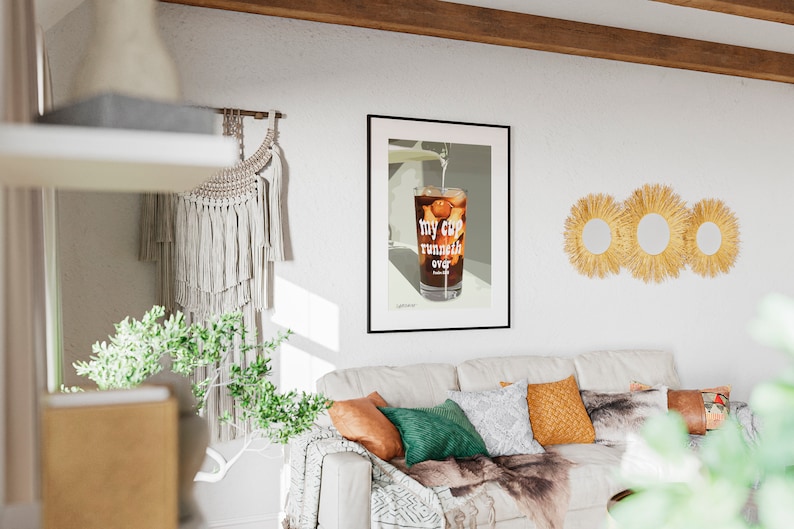 Pu&ograve; includere: Una stampa incorniciata di un bicchiere di caff&egrave; freddo con il testo "my cup runneth over" in un soggiorno con un divano bianco, una coperta e cuscini.