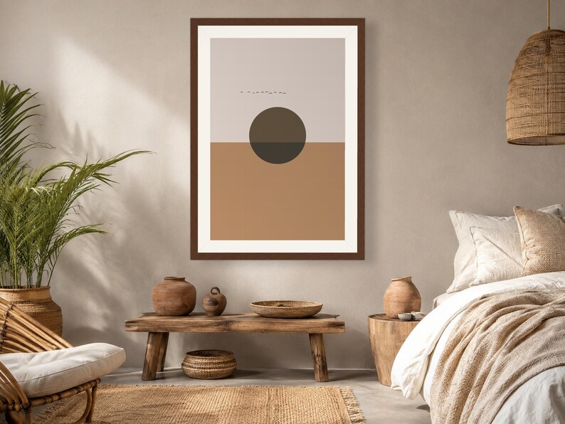 May include: A framed wall art print featuring a horizontal split composition with a light beige upper section and a solid tan lower section. A dark brown circle is centered over the horizon line, and a small row of birds is visible in the sky.
