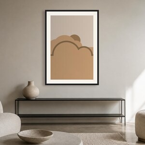 May include: A framed wall art print featuring a graphic illustration of layered, rounded shapes in shades of tan, beige, and brown. The artwork is enclosed in a thin black frame and displays a stylized landscape composition with curved lines.