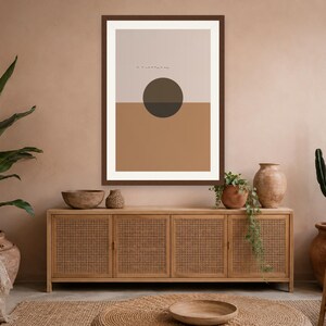 May include: A framed wall art print featuring a horizontal split design with a light beige upper section and a solid terracotta lower section. A dark brown circle is centered over the horizon line, with small, thin black horizontal lines above it.