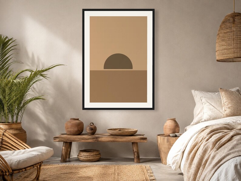 May include: A framed wall art print featuring a minimalist graphic design of a dark brown semi-circle sun rising over a solid medium brown horizon line, set against a light tan background, enclosed within a thin black rectangular frame.