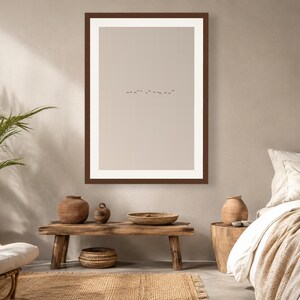 May include: A framed wall art print featuring a minimalist beige background with a small, centered horizontal line of tiny black birds in flight. The artwork is enclosed in a dark brown rectangular frame with a wide white mat border.