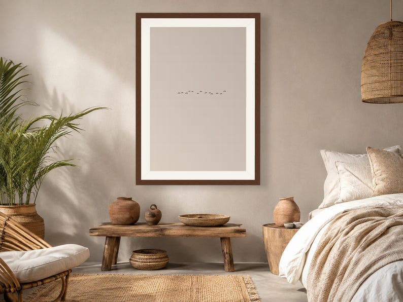 May include: A framed wall art print featuring a minimalist beige background with a small, centered horizontal line of tiny black birds in flight. The artwork is enclosed in a dark brown rectangular frame with a wide white mat border.