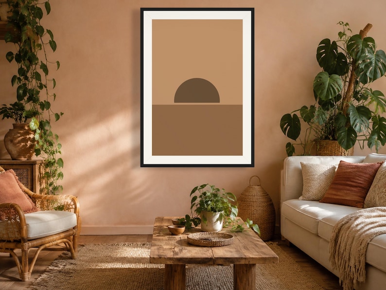 May include: A framed wall art print featuring a minimalist graphic design of a dark brown semi-circle sun rising over a solid medium brown horizon line, set against a light tan background, enclosed within a thin black rectangular frame.
