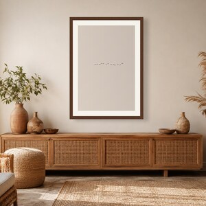 May include: A rectangular wall art print featuring a minimalist beige background with a small, horizontal line of tiny black birds flying in the center, enclosed within a dark brown frame with a wide white mat border.