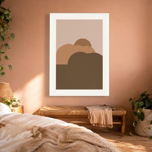 Puede incluir: Una impresi&oacute;n de arte mural enmarcada que presenta una composici&oacute;n de paisaje abstracto minimalista. La obra muestra formas redondeadas superpuestas en varios tonos de marr&oacute;n, bronceado y beige, sobre un fondo gris pardo en un marco blanco.