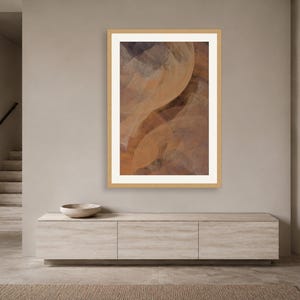 May include: A vertical framed wall art piece featuring an abstract composition of overlapping, translucent curved shapes in shades of warm tan, deep brown, and muted gray, enclosed within a light-colored wooden frame and a white mat border.