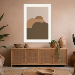 Puede incluir: Una l&aacute;mina de arte mural rectangular en un marco blanco que presenta una composici&oacute;n abstracta de formas redondeadas superpuestas en tonos beige, tostado y marr&oacute;n oscuro. La obra se exhibe en una pared sobre un aparador de madera.