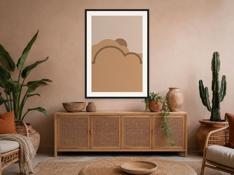 May include: A framed wall art print featuring a minimalist abstract landscape with layered, rounded shapes in shades of tan, beige, and brown. The composition includes a semi-circular sun element partially obscured by cloud-like forms in a flat design.