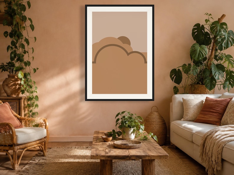 May include: A framed wall art print featuring a graphic illustration of layered abstract shapes in shades of tan, beige, and brown. The design includes curved, cloud-like forms and a semi-circular sun element set against a solid light background.