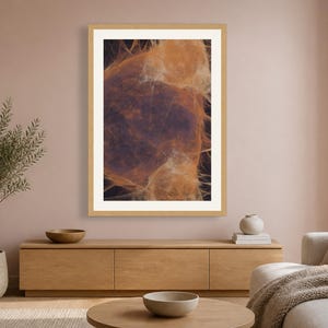 May include: A rectangular wall art print featuring an abstract composition of wispy, translucent orange and amber fibers set against a deep, dark background, enclosed within a simple light-toned wooden frame with a wide white mat border.