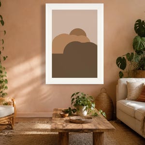 Puede incluir: Una impresi&oacute;n de arte mural rectangular que presenta un dise&ntilde;o de paisaje abstracto minimalista con formas redondeadas superpuestas en tonos beige, marr&oacute;n claro y marr&oacute;n oscuro, dentro de un marco blanco, en formato vertical.