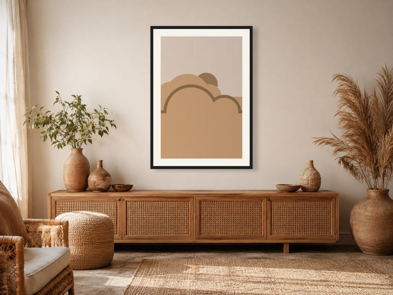 May include: A framed wall art print featuring a minimalist abstract landscape with layered shapes in shades of beige, tan, and brown. The composition includes a semi-circular sun element partially obscured by rounded cloud-like forms in a flat design.
