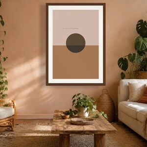 May include: A rectangular wall art print in a dark brown frame featuring a split-color design with a light beige upper half and a medium brown lower half. A dark brown circle is centered over the horizontal line, with small black line art above.