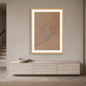 May include: A framed wall art piece featuring a light brown background with thin, intersecting dark lines that create a subtle, abstract geometric pattern. The artwork is enclosed in a light-colored wooden frame with a wide white mat border.