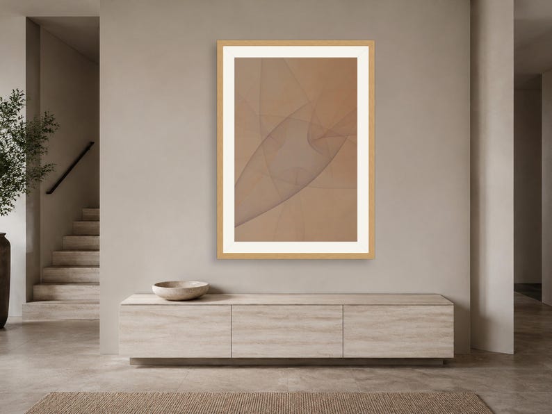 May include: A framed wall art piece featuring a light brown background with thin, intersecting dark lines that create a subtle, abstract geometric pattern. The artwork is enclosed in a light-colored wooden frame with a wide white mat border.