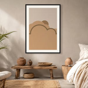 May include: A framed wall art print featuring a stylized landscape with layered abstract shapes in shades of tan, beige, and brown. The composition includes rounded cloud-like forms and a semi-circular sun element set against a neutral background.