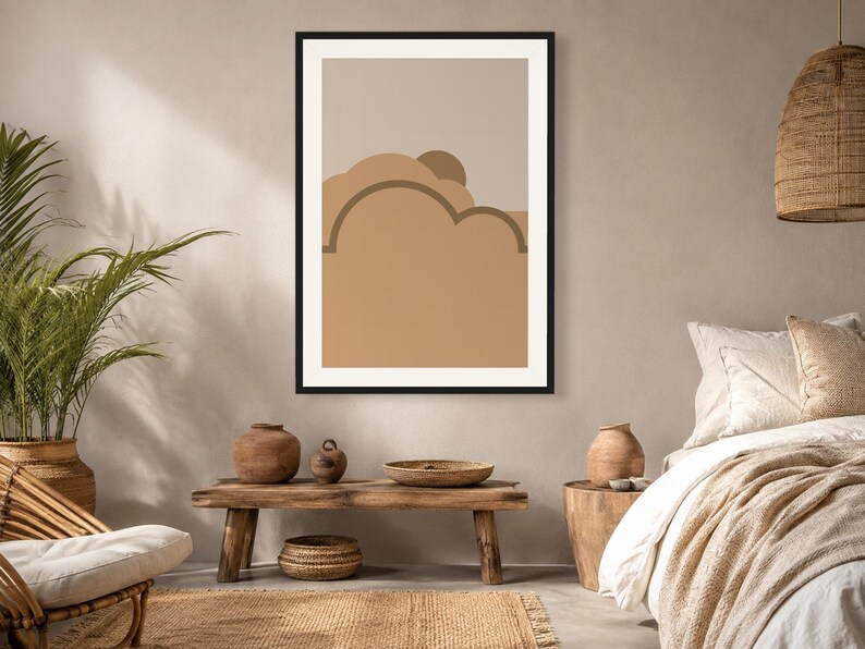 May include: A framed wall art print featuring a stylized landscape with layered abstract shapes in shades of tan, beige, and brown. The composition includes rounded cloud-like forms and a semi-circular sun element set against a neutral background.