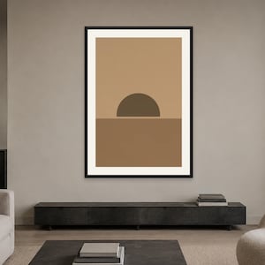 May include: A framed wall art print featuring a geometric landscape design. The artwork displays a dark brown semi-circle positioned on a horizontal line, separating a light tan upper section from a medium brown lower section, all within a black frame.