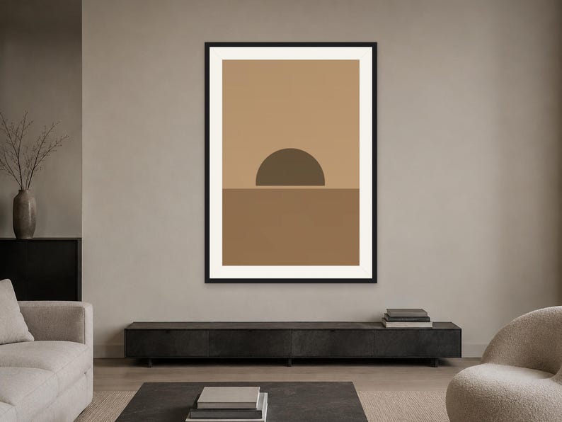 May include: A framed wall art print featuring a geometric landscape design. The artwork displays a dark brown semi-circle positioned on a horizontal line, separating a light tan upper section from a medium brown lower section, all within a black frame.