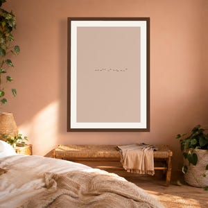 May include: A framed wall art print featuring a minimalist composition with a solid light beige background and a small, horizontal line of tiny black birds flying in the center, enclosed within a dark brown frame and a wide white mat border.