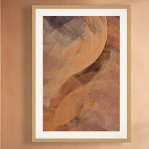 May include: A rectangular wall art print in a light wood frame with a white mat. The artwork features an abstract composition of swirling, translucent layers in shades of burnt orange, deep brown, and muted gray, creating a fluid, layered effect.