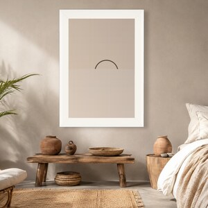 May include: A framed wall art print featuring a minimalist graphic design of a dark brown semi-circle arching over a horizontal line, set against a solid light beige background. The artwork is enclosed in a thick white frame and mounted on a wall.