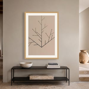 May include: A framed wall art print featuring a light beige background with a black line drawing of a stylized tree branch. The artwork is enclosed in a light-colored wooden frame with a white mat border, displaying a clean and simple graphic design.