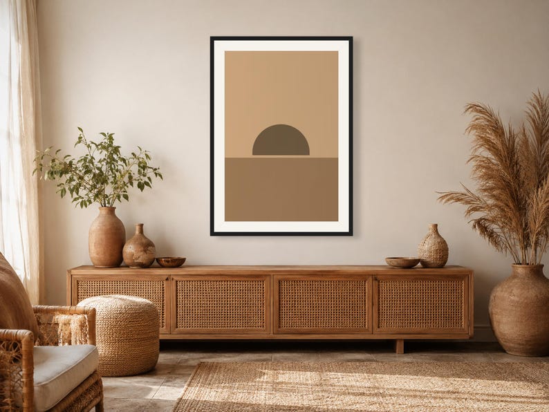 May include: A framed rectangular wall art print featuring a minimalist graphic design of a dark brown semi-circle sun resting on a horizon line, set against a light tan background with a medium brown lower section, enclosed in a black frame.
