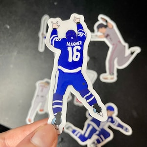 May include: A blue and white hockey player sticker with the name "Marner" and the number "16" on the back. The player is in a celebratory pose with arms raised.
