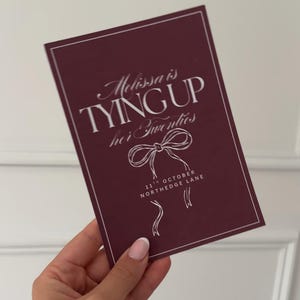 Peut inclure: Une carte d'invitation bordeaux avec du texte blanc. On peut lire "Melissa is Tying Up Her Twenties", ainsi que la date du "11 octobre" et le lieu "North Edge Lane".