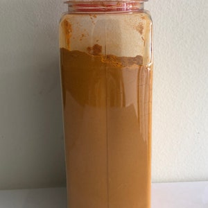 May include: A clear plastic jar with a red lid filled with yellow turmeric powder.