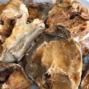 May include: A close-up of a pile of dried fish, with a light brown and white color. The fish is arranged in a white dish.