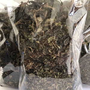 May include: A clear plastic bag filled with dried green leaves. The leaves are loose and appear to be a type of herb.