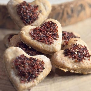 Könnte beinhalten: Eine Ansammlung von herzförmigen Keksen in hellbrauner Farbe. Jeder Keks ist mit einer großzügigen Menge rotbrauner Streusel bedeckt. Die Kekse liegen auf einer Holzoberfläche.