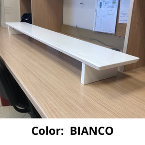 May include: White monitor stand made of wood. The stand is on a wooden desk. Color: BIANCO