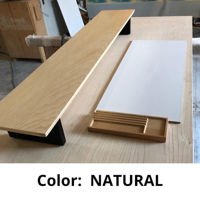 May include: A natural wood desk shelf with black metal brackets. The shelf is mounted on a natural wood desk surface. The desk has a white surface and a small wooden tray with dividers.