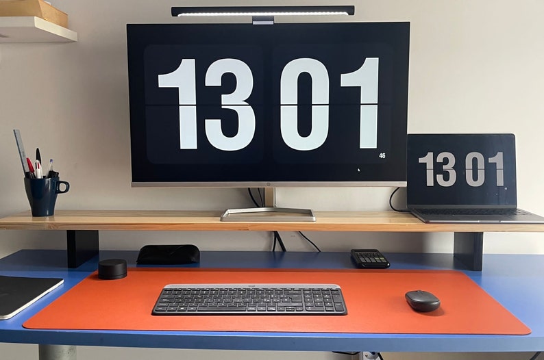 May include: A home office desk with a computer monitor, laptop, keyboard, mouse, and a cup of pens. The monitor and laptop both display the time 13:01.