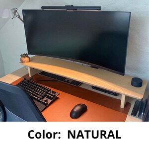 May include: A curved monitor sits on a natural wood monitor stand. The stand is on a desk with a keyboard, mouse, and a brown desk mat. The text "Color: NATURAL" is visible at the bottom of the image.