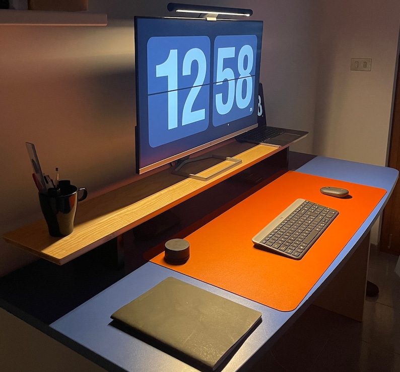 May include: A desk workspace with a computer monitor displaying the time "12:58", a keyboard, a notebook, and a lamp.
