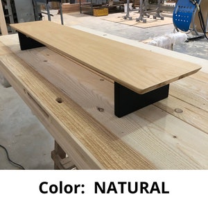 May include: A natural wood shelf with black metal brackets. The shelf is sitting on a wooden surface. Color: NATURAL