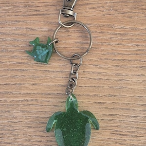 Llavero de tortuga hecho a mano con plástico reciclado del océano y resina epoxi. Cada venta financia la limpieza del océano. Viene en una caja de regalo de cartón.