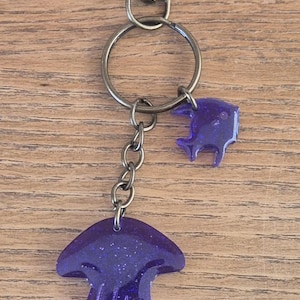 Portachiavi a forma di medusa realizzato a mano con plastica oceanica riciclata e resina epossidica. Ogni vendita finanzia la pulizia dell'oceano. L'articolo viene consegnato in una scatola regalo di cartone.