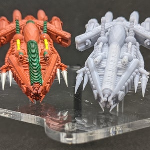 Può includere: Due astronavi in miniatura dettagliate, una dipinta di rosso con accenti verdi e l'altra in grigio, sono esposte su un supporto in acrilico trasparente.