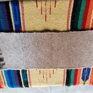 May include: A beige woven rug with a colourful striped pattern on either side. The rug is made of natural fibres and has a rustic look.