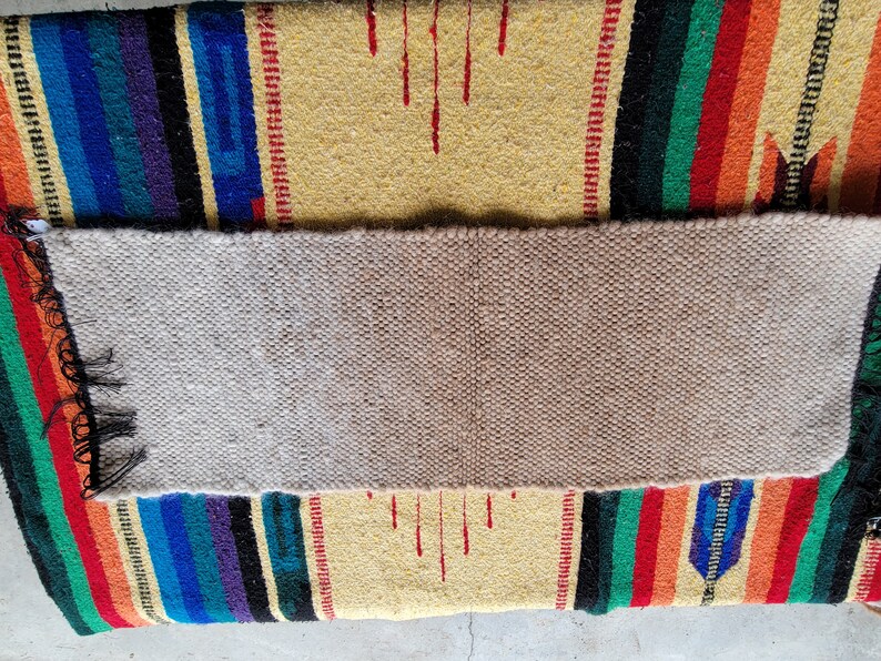 May include: A beige woven rug with a colourful striped pattern on either side. The rug is made of natural fibres and has a rustic look.