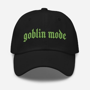 May include: Black baseball cap with the words "goblin mode" embroidered in green gothic lettering across the front. The cap has a curved brim and a rounded crown.