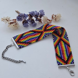 Puede incluir: Una pulsera de cuentas con un diseño de arcoíris. La pulsera está hecha de pequeñas cuentas rojas, naranjas, amarillas, verdes, azules, moradas y negras. Tiene un cierre y una cadena plateados, y mide unos 15 cm de largo.