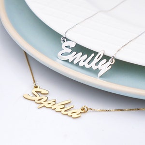 May include: Two personalized necklaces with the names "Emily" and "Sophia" in a cursive font. The necklaces are on a white surface with a light blue plate behind them.
